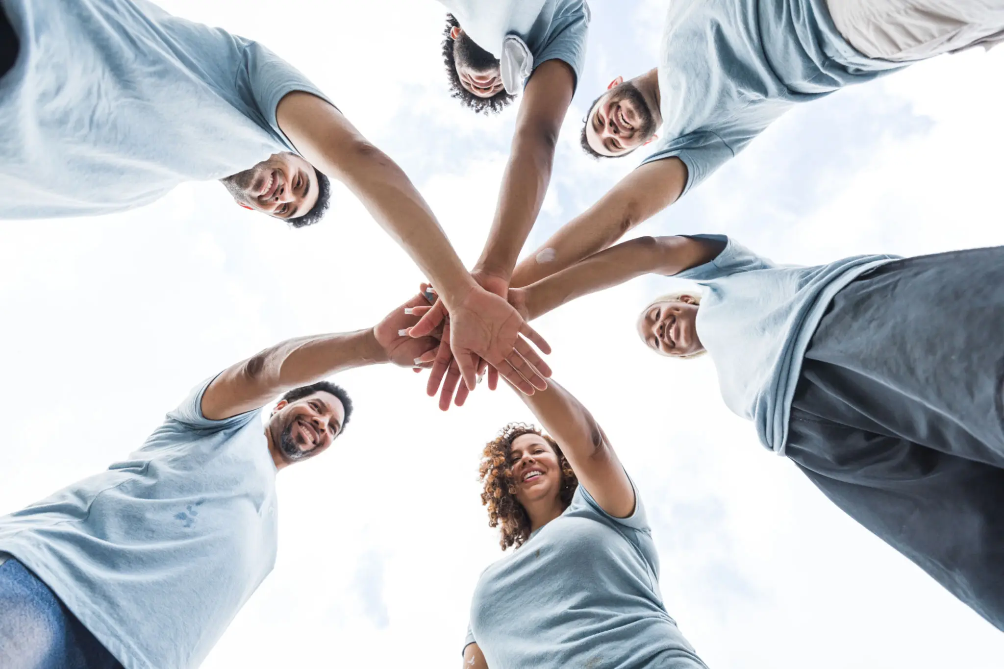 Group of people joining hands in unity from below.
