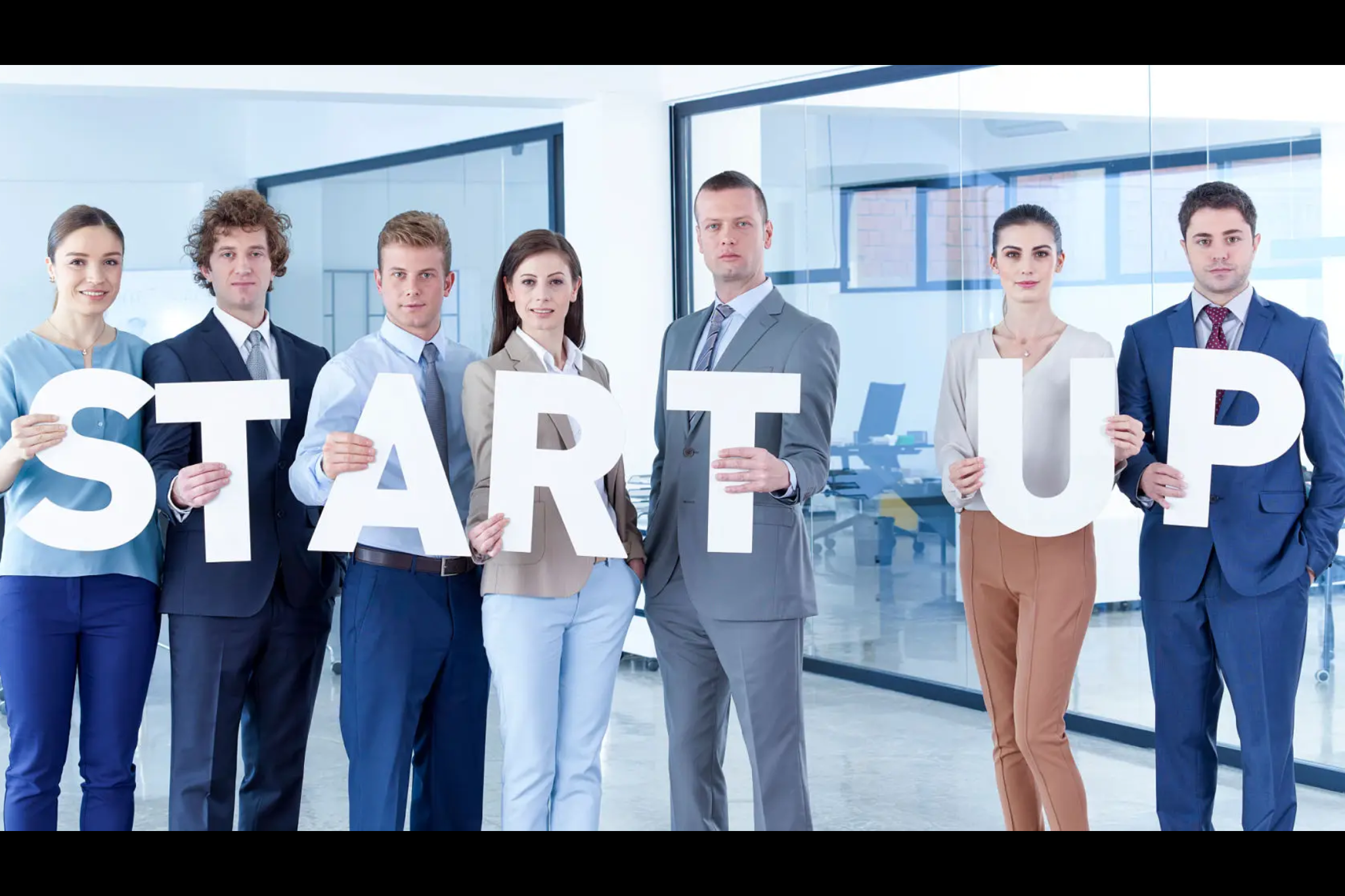 A group of professionals holding letters spelling 'START UP' in an office.